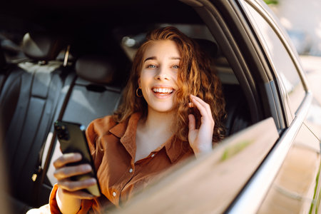 A young woman with a smartphone chats in the back seat of a car. Transport concept. Lifestyle.の写真素材