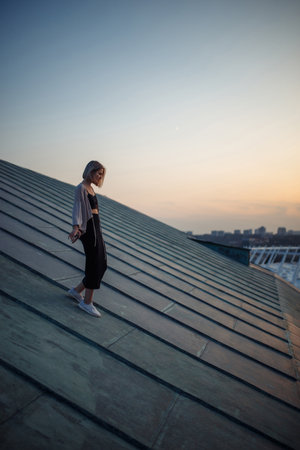 Beautiful woman on rooftop posing at sunset. Woman enjoys atmosphere of city of freedom. Relaxation.の写真素材