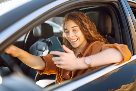 Happy woman in the car in the driver's seat looks at the smartphone. Business, technology concept.の写真素材