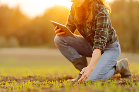 Farmer woman in boots checks the quality of the soil before sowing in her hands with digital tablet.
