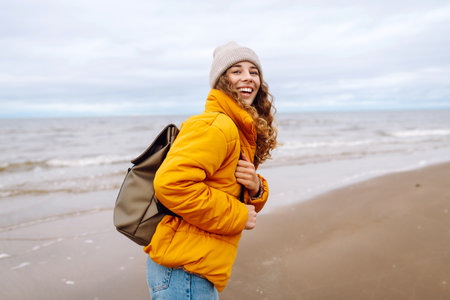 A beautiful young tourist woman in a yellow jacket with a backpack enjoys life near the sea.