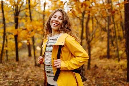Hiking in autumn forest. Smiling tourist in bright coat walks through autumn park in sunny weather.