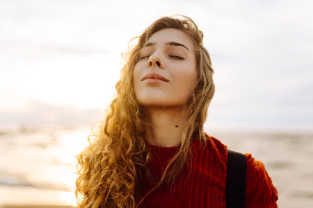 As she walked along the beach, the woman tourist adjusted her backpack, taking in the salty sea airの写真素材