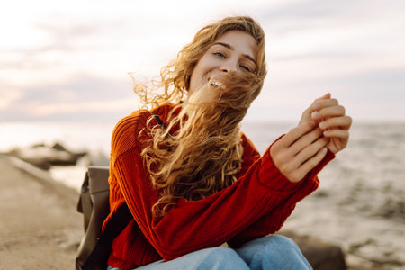 Portrait of woman enjoying a breezy day near a vibrant red lighthouse at sunset. Lifestyle concept.の写真素材
