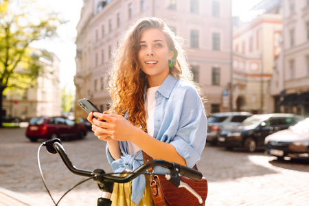 Young woman using mobile phone while riding bicycle at the city street outdoor. Selfie time.の写真素材