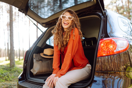 A traveler young woman smiles while sitting in the trunk of her car during a sunny day in a forestの写真素材