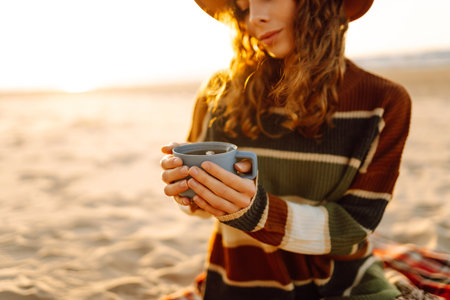 Lonely romantic woman drinking coffee looking at sunset at picnic on the beach. Lifestyle concept.の写真素材