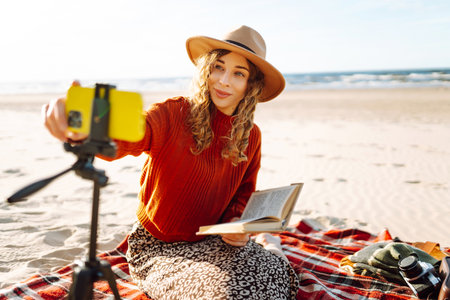 Young woman sits on the beach and records a video for her subscribers. Blogging, technology conceptの写真素材