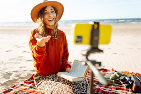 Young woman sits on the beach and records a video for her subscribers. Blogging, technology conceptの写真素材
