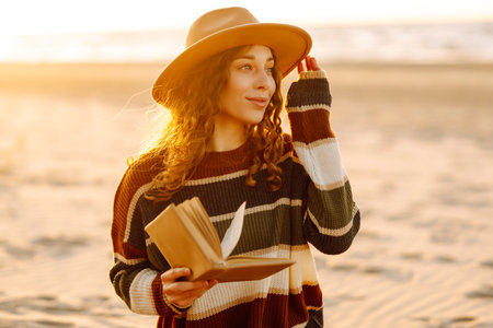Romantic woman reading book sit on plaid have picnic outdoors on sea sand beach backgroundの写真素材