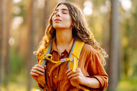 Tourist woman hiking alone in thick autumn forest. Stylish female looks for pathway among trees.の写真素材