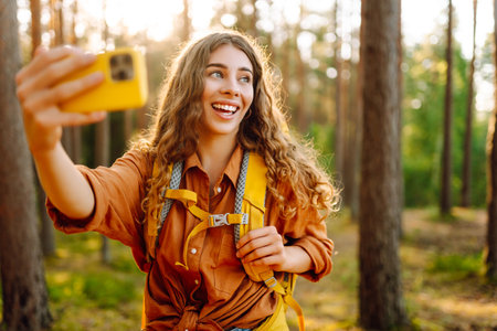Beautiful woman taking picture of herself while walking in sunny forest. Selfie in nature. Adventureの写真素材