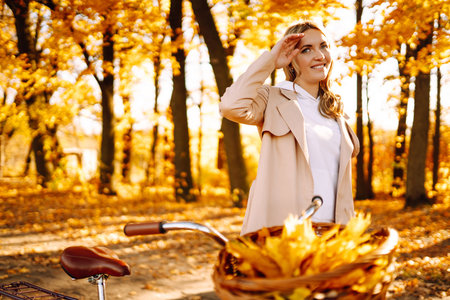 Stylish woman with a bicycle enjoying autumn weather in the park. Beautiful Woman in the autumn forest.の写真素材
