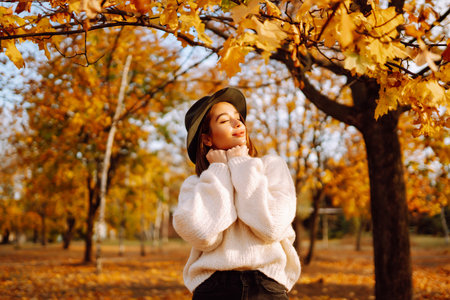 Autumn woman. Young cheerful woman in white sweater and hat walks in the nature park on a sunset.の写真素材