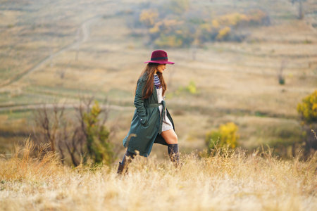 Beautiful stylish girl walks in the autumn park. The girl is dressed in a green coat and a red hat.の写真素材