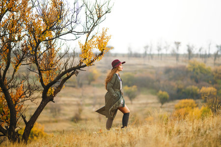 Beautiful stylish girl walks in the autumn park. The girl is dressed in a green coat and a red hat.