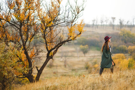 Beautiful stylish girl walks in the autumn park. The girl is dressed in a green coat and a red hat.の写真素材