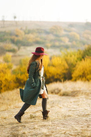 Beautiful stylish girl walks in the autumn park. The girl is dressed in a green coat and a red hat.の写真素材