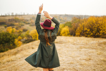 Beautiful stylish girl walks in the autumn park. The girl is dressed in a green coat and a red hat.の写真素材