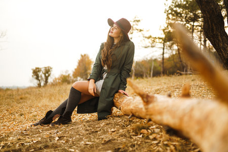 Beautiful stylish girl walks in the autumn park. The girl is dressed in a green coat and a red hat.