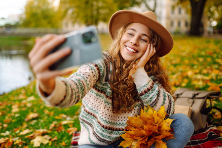 Stylish woman takes selfie on phone in autumn forest, communicates via video call. Concept of nature