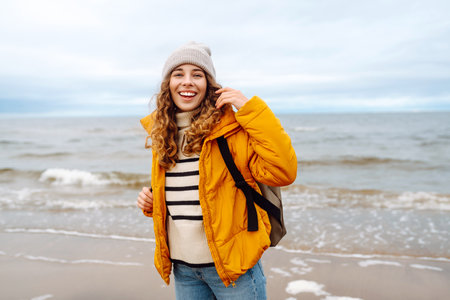 A beautiful young tourist woman in a yellow jacket with a backpack enjoys life near the sea. Travel.