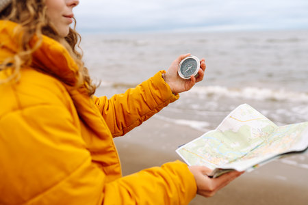 Traveler explorer young woman holding compass, map in hands on beach near the sea. Active lifestyle.の写真素材