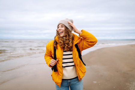 A beautiful young tourist woman in a yellow jacket with a backpack enjoys life near the sea. Travel.