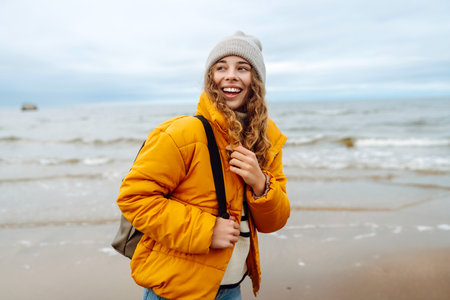 A beautiful young tourist woman in a yellow jacket with a backpack enjoys life near the sea. Travel.の写真素材