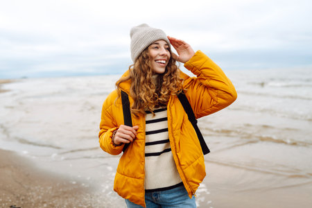 A beautiful young tourist woman in a yellow jacket with a backpack enjoys life near the sea. Travel.の写真素材