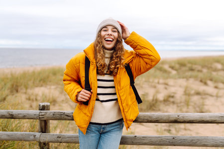 A beautiful young tourist woman in a yellow jacket with a backpack enjoys life near the sea. Travel.