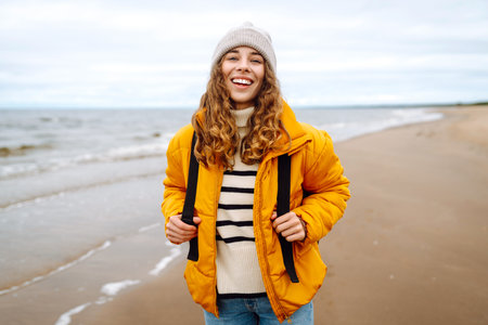 A beautiful young tourist woman in a yellow jacket with a backpack enjoys life near the sea. Travel.