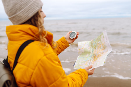 Traveler explorer young woman holding compass, map in hands on beach near the sea. Active lifestyle.