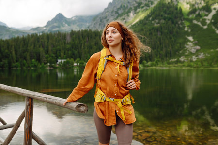 Female traveler with hiking backpack poses against backdrop of mountain lake. Adventure concept.の写真素材