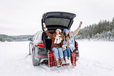 Two young women near a car on a snowy road. Traveling in Winter.の写真素材
