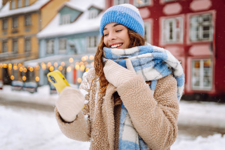 Young woman walking in winter street, holding using smart phone. Online communication.の写真素材