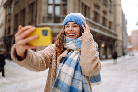 Young woman in winter time using phone outside the street. Selfie time. Holidays, rest, blogging.の写真素材