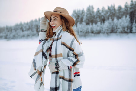 Happy woman in a hat and scarf walks near a winter lake in the winter forest. Winter walk concept.の写真素材