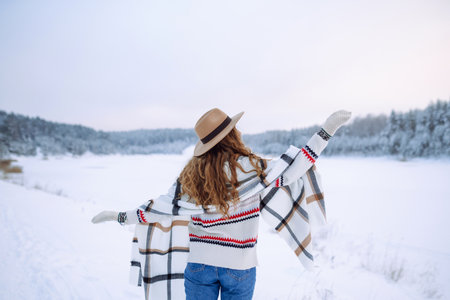 Happy woman in a hat and scarf walks near a winter lake in the winter forest. Winter walk concept.の写真素材
