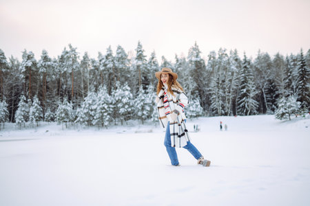 Happy woman in a hat and scarf walks near a winter lake in the winter forest. Winter walk concept.の写真素材
