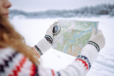 Curly-haired young woman standing in the wild with a map and compass in a snowy forest.の写真素材