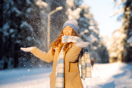 Young woman in warm clothes plays with snow on a sunny winter day. Concept of walking, fun.の写真素材