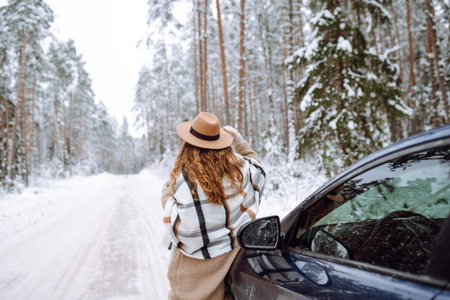 Beautiful young woman near a car in a snowy forest. First snow, great mood. Concept of vacation.の写真素材
