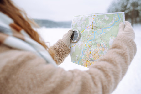 Beautiful woman traveler holds a compass and map in hands. Enjoying winter travel. Active lifestyle.の写真素材