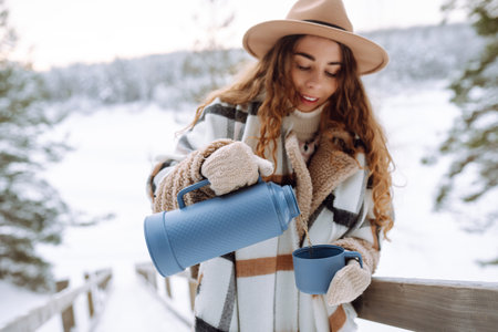 Young woman drinks hot tea while holding a thermos in nature. . Vacation conceptの写真素材