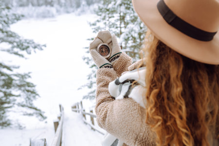 Woman in a hat holding a compass lying in hand on mitten against backdrop of snowy winter forest.の写真素材