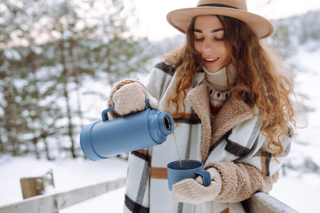 Young woman drinks hot tea while holding a thermos in nature. . Vacation conceptの写真素材