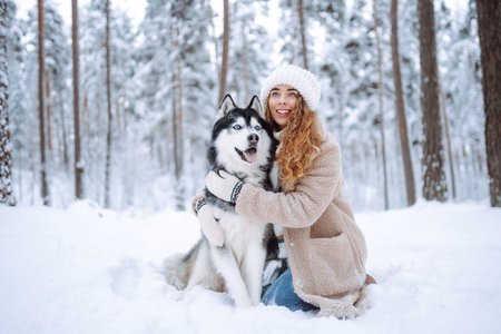 Cute woman spends time with her husky dog in the winter snowy forest. Lifestyle.の写真素材