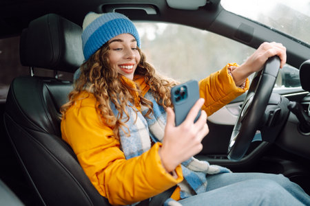 Stylish woman sitting in car dressed in winter clothes using smartphone.