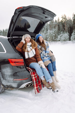 Two young women near a car on a snowy road. Traveling in Winter.の写真素材